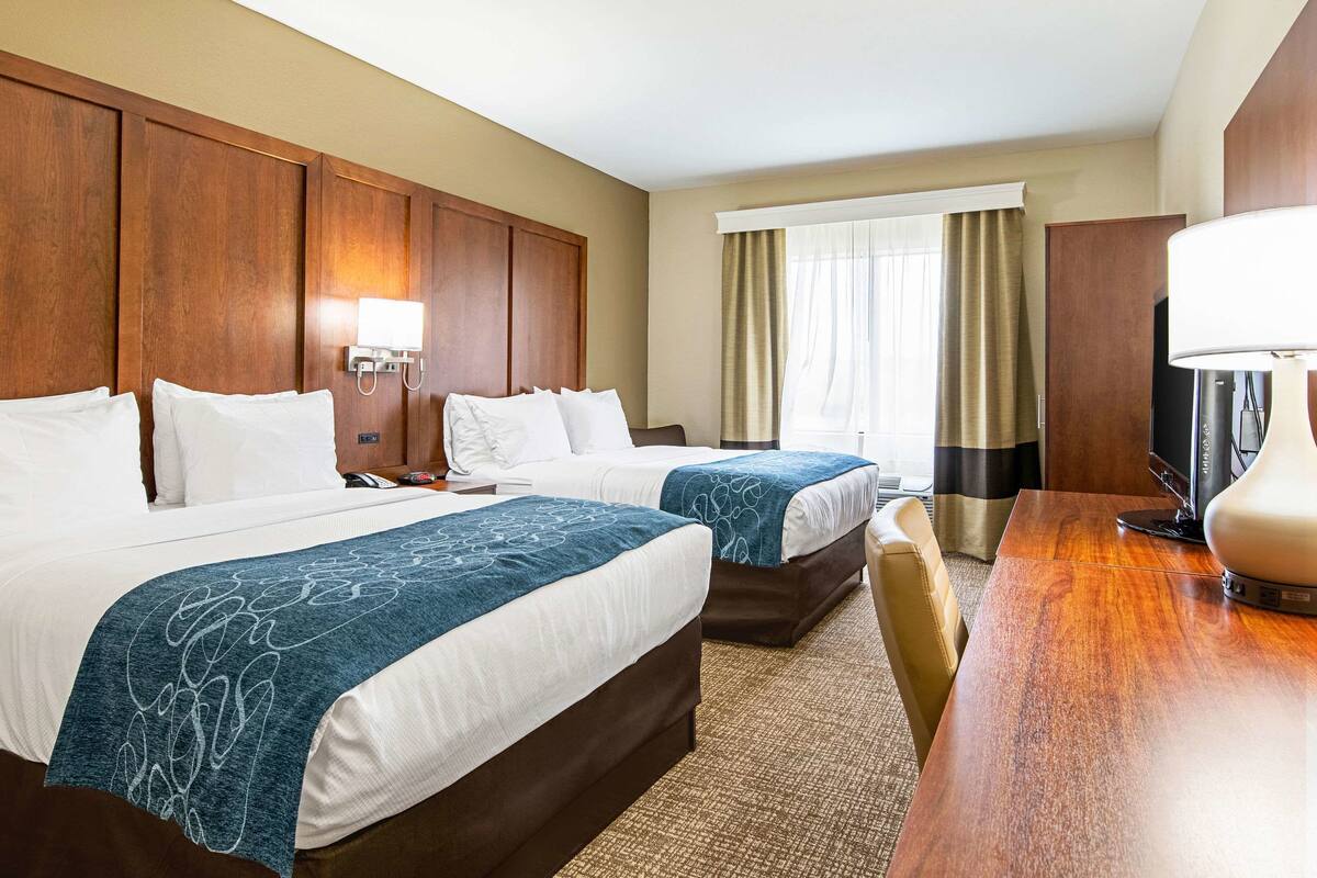 Ein Hotelzimmer mit zwei Betten, einem hölzernen Kopfteil, einem Schreibtisch mit Lampe und einem Fernseher.
