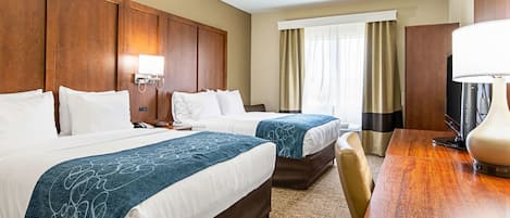 A hotel room with two beds, a wooden headboard, a desk with a lamp, and a television.
