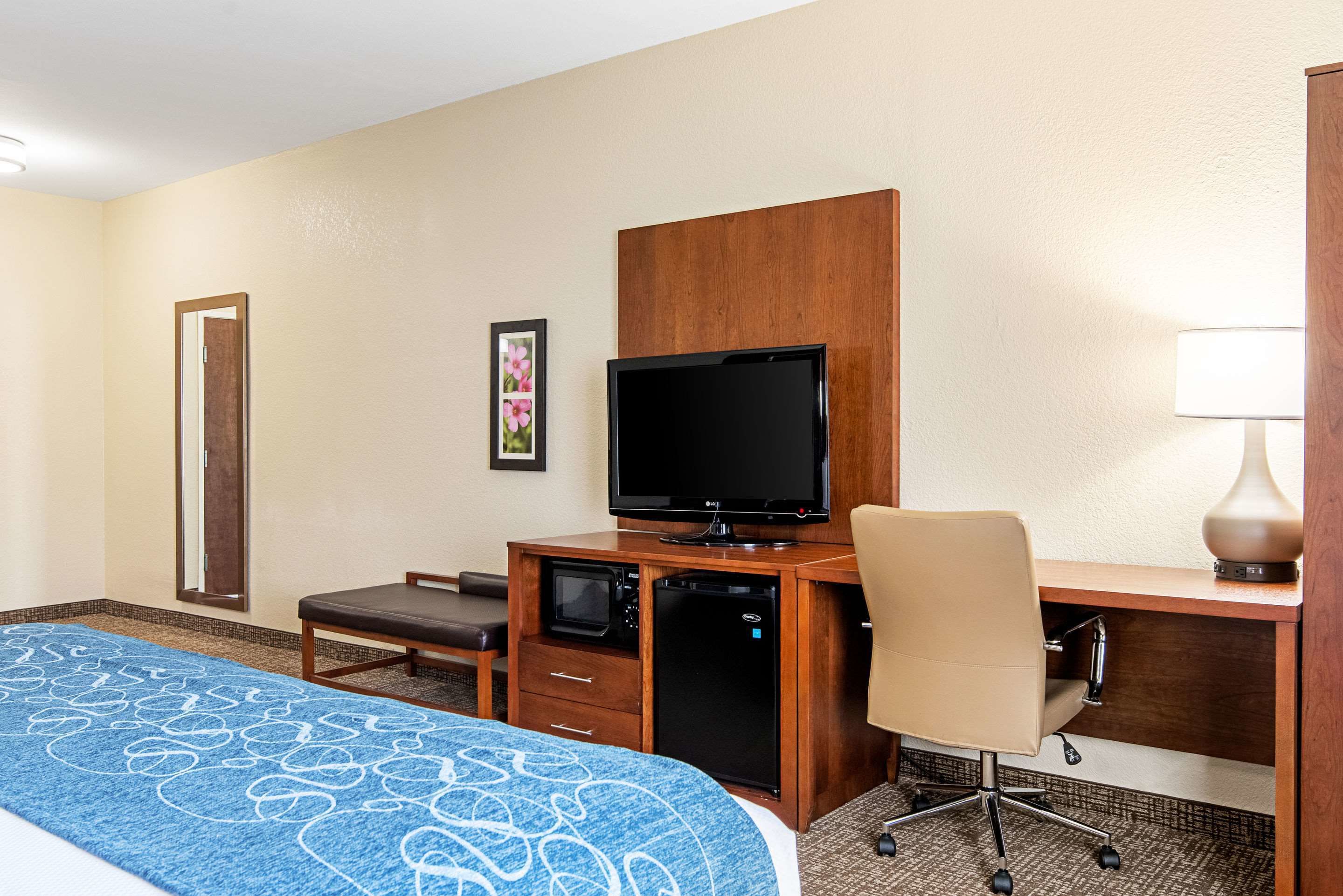 Ein Hotelzimmer mit einem Bett, einem Schreibtisch mit Computer, einem Fernseher, einer Mikrowelle und einem Sessel.