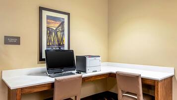 A business center with a white desk, a laptop, a printer, and two chairs.