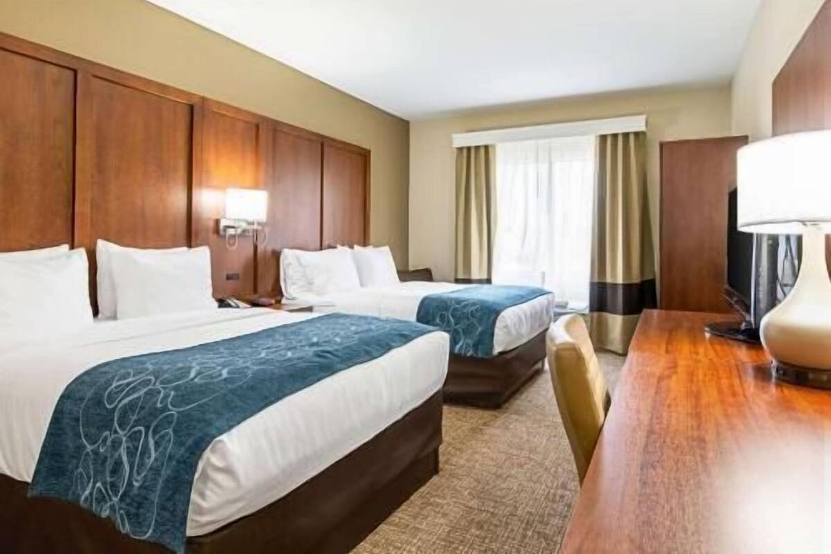 Ein Hotelzimmer mit zwei Betten, einem Schreibtisch, einem Fernseher und einem Fenster mit Vorhängen.