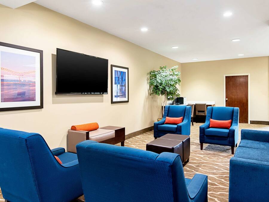 A hotel lobby with blue seating, a flat-screen TV, framed pictures, and a potted plant.