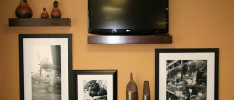 Un televisor de pantalla plana montado en la pared, sobre un estante de madera con jarrones decorativos y fotografías blanco y negro enmarcadas.