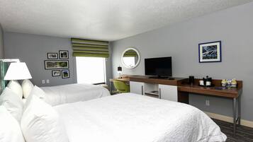 Habitación de hotel con dos camas, un escritorio con televisor, cafetera y una silla.