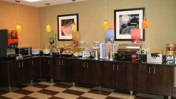 Un mostrador de buffet con diferentes alimentos y bebidas, un mostrador de recepción y cuadros en la pared.
