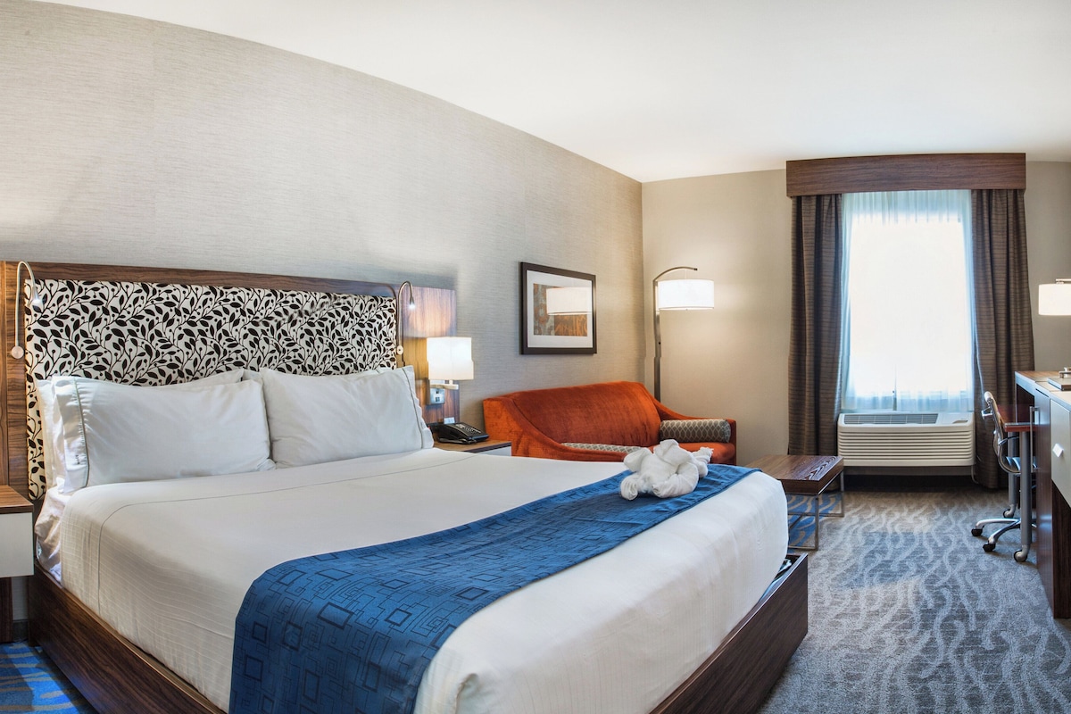 Quarto de hotel com cama grande, escrivaninha, cadeira e televisão.