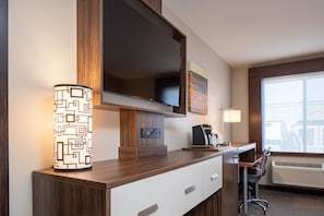 Quarto de hotel com televisão de tela plana fixada sobre uma escrivaninha de madeira, cafeteira, cadeira e janela com unidade de ar condicionado.