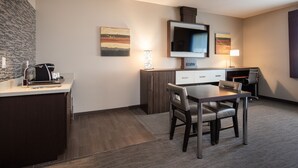 Una habitación de hotel moderna con kitchenette, un comedor con mesa y sillas, un televisor de pantalla plana montado en la pared y obras de arte en las paredes.