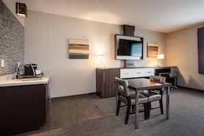 Quarto de hotel moderno com cozinha compacta, área de jantar com mesa e cadeiras, TV de tela plana na parede e obras de arte nas paredes.