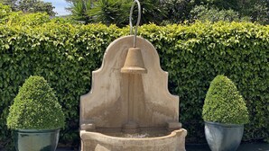Una fuente de piedra con una campana, rodeada de setos podados.
