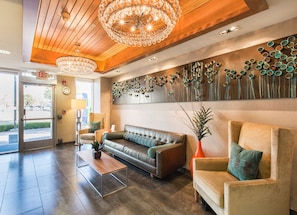 A lobby with a leather sofa, a coffee table, a reception desk, and a wall with a decorative metal art piece. - Holiday Inn Express Redwood City-Central by IHG (Redwood City)