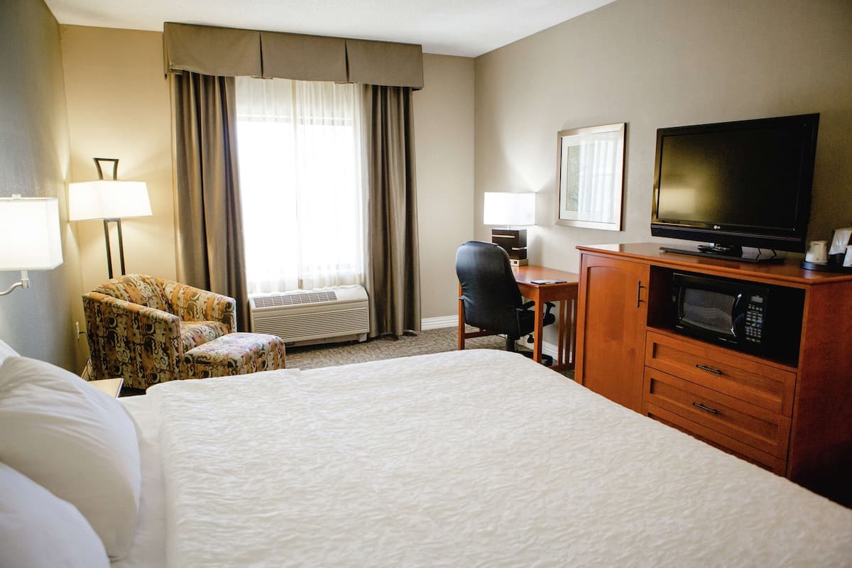 A hotel room with a large bed, a desk with a computer, a television, a microwave, and two chairs.
