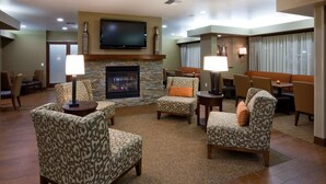 A spacious lobby with patterned armchairs, a stone fireplace, a flat-screen TV, and a dining area with tables and chairs. - Hampton Inn Mitchell (Mitchell)