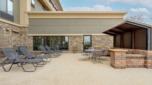 An outdoor patio with lounge chairs and a barbecue area, stone walls, and a covered seating area. - Hampton Inn Mitchell (Mitchell)