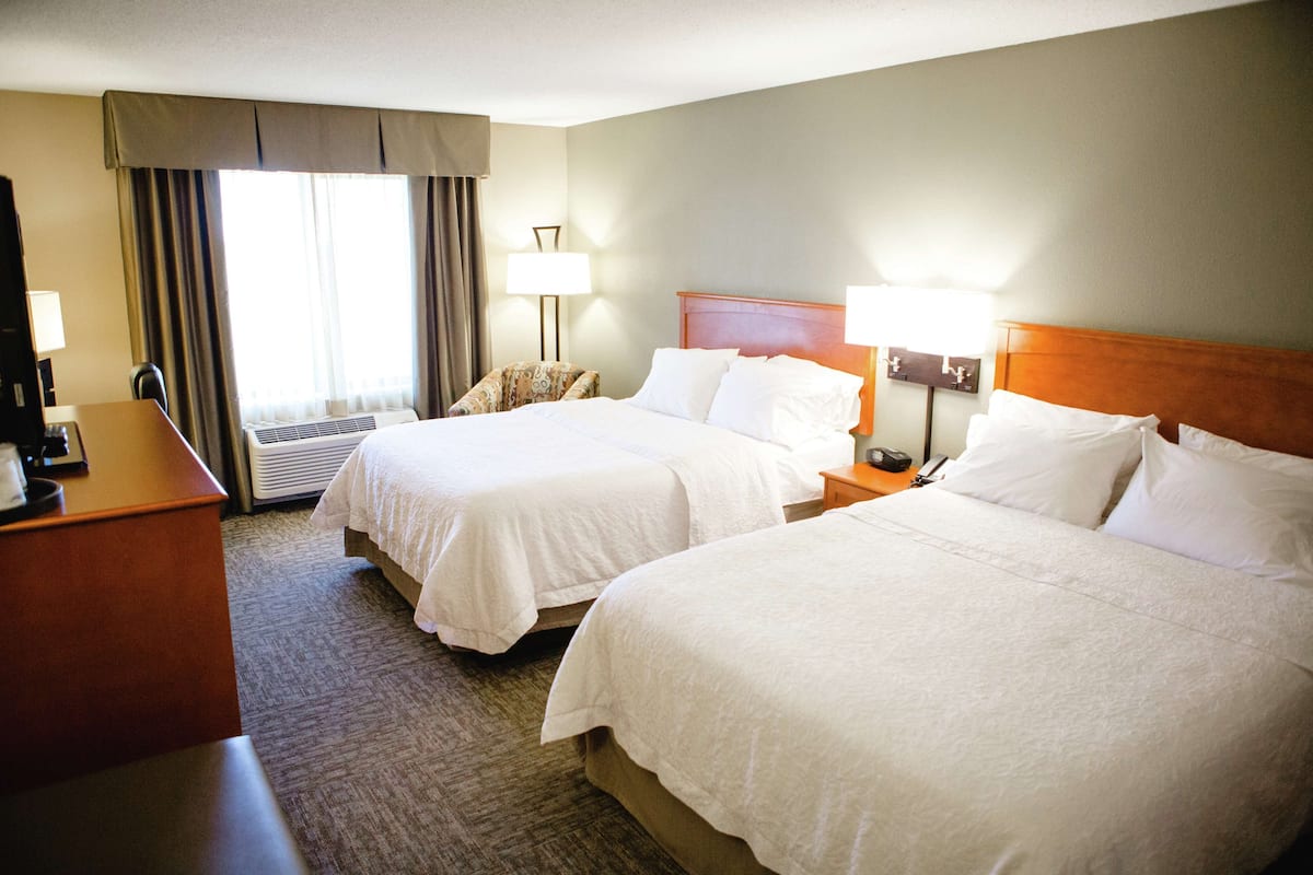 A hotel room with two beds, a desk, a chair, and a window with curtains.