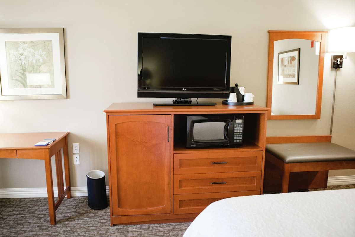 A hotel room with a wooden desk, a television, a microwave, a bed, and a trash can.