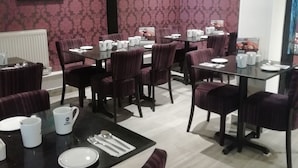 Un espace repas avec des tables dressées, agrémenté de chaises en bois foncé et d’un papier peint à motifs.
