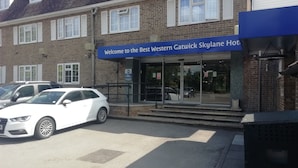 L’entrée d’un hôtel, avec une enseigne bleue sur laquelle on peut lire : « Bienvenue au Best Western Gatwick Skylane Hotel ».