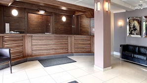 Un espace d’accueil comprenant un comptoir de réception en bois, un canapé en cuir noir et un sol carrelé.