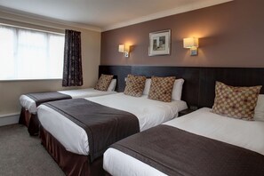 Ein Hotelzimmer mit drei Betten, jedes mit brauner Bettdecke und weißen Laken. Zwei Wandleuchten und ein gerahmtes Bild hängen über den Betten.