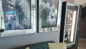 Un canapé en cuir noir avec deux coussins, un miroir fixé au mur et un distributeur automatique de boissons.
