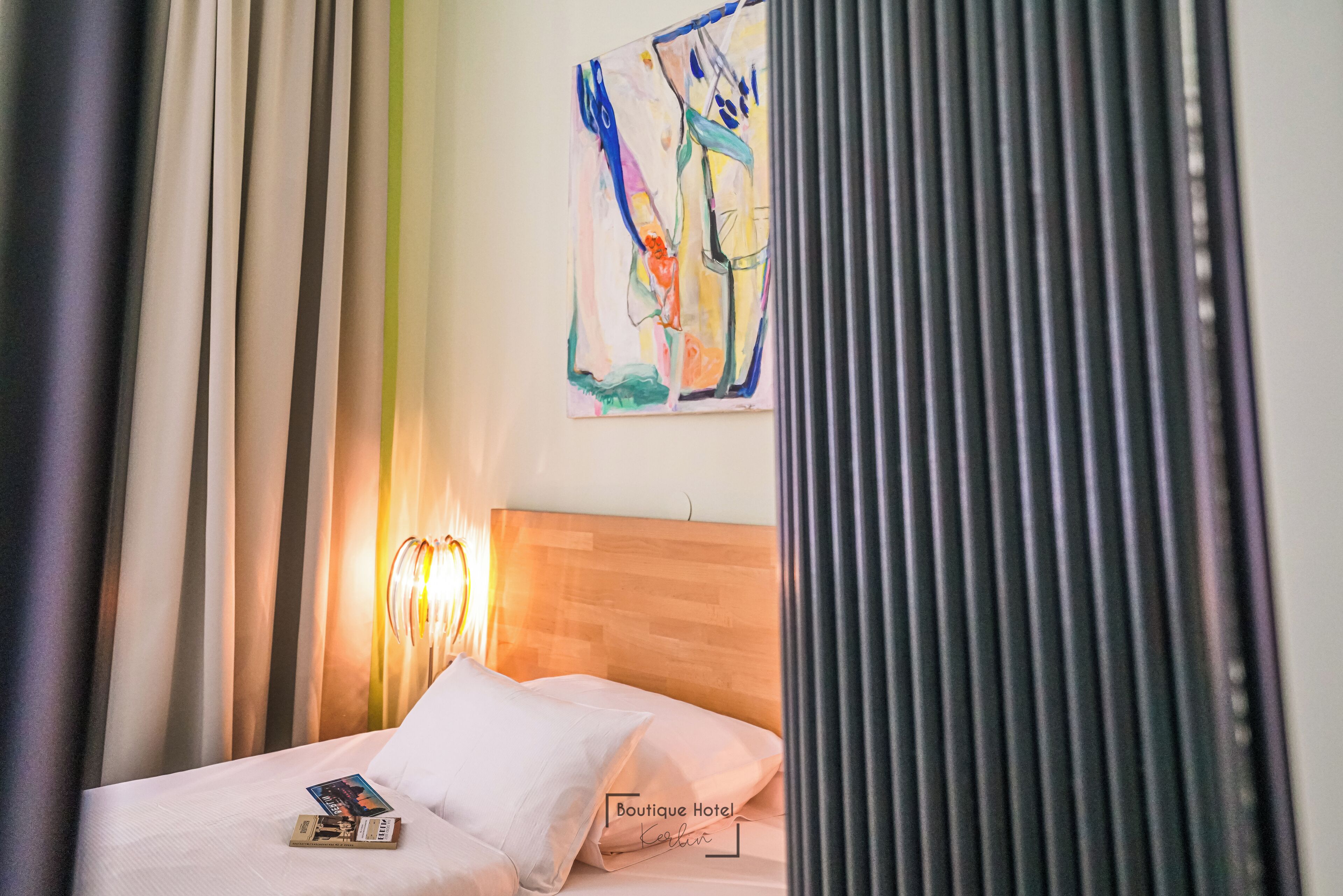 A hotel room with a bed, a painting on the wall, and a lamp.