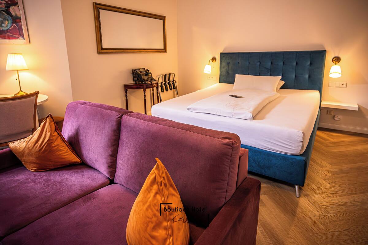 Ein Hotelzimmer mit einem Bett, einem violetten Sofa und Holzboden.