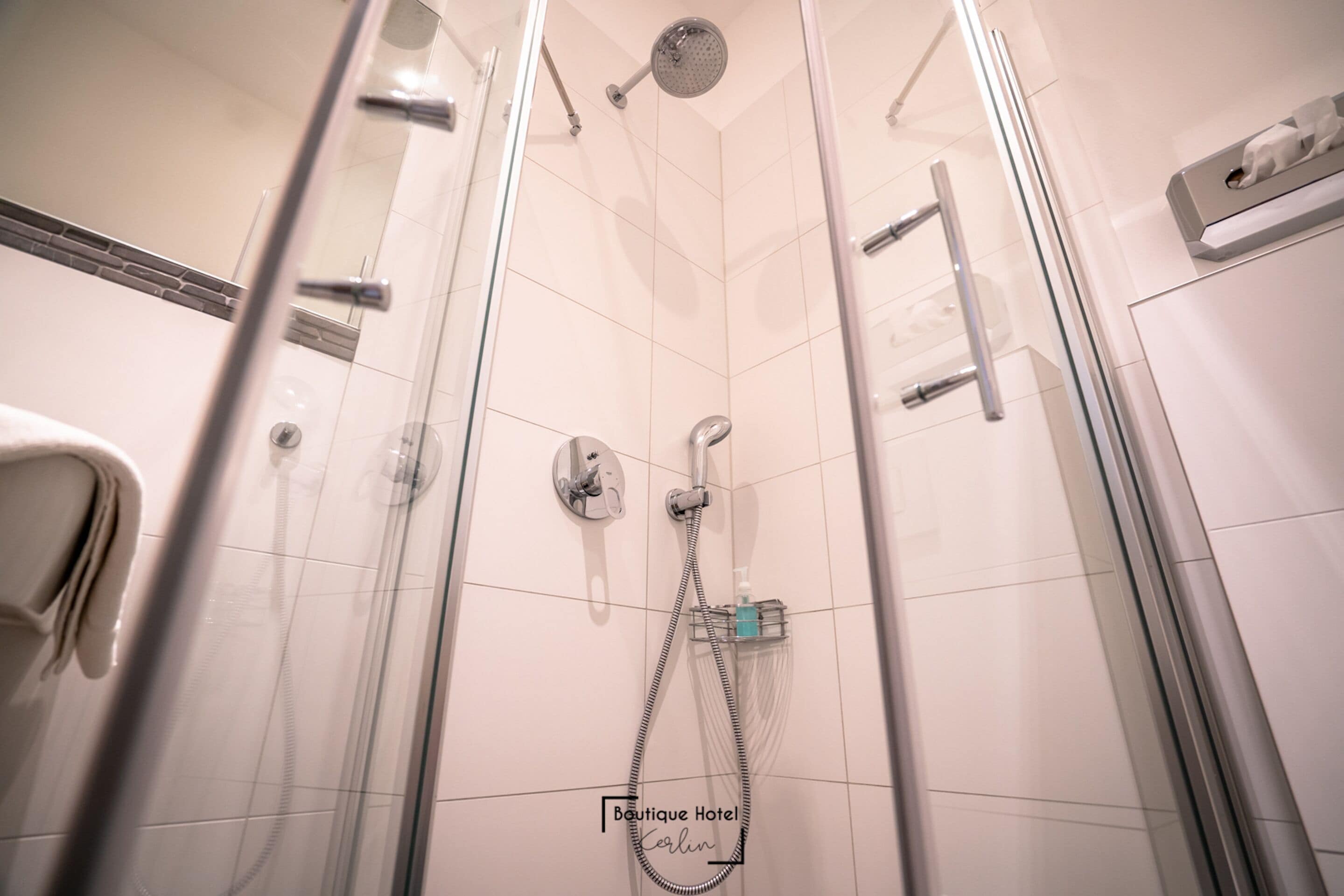A glass-enclosed shower with a handheld showerhead, a wall-mounted faucet, and a handheld showerhead.