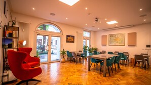 A hotel lobby with a herringbone wooden floor, red and teal chairs, and a large window with a view of the street. - Boutique Hotel Kerlin (Berlin)