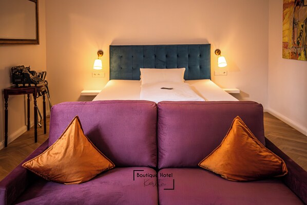 A hotel room with a bed, a purple sofa with two pillows, and a nightstand with a lamp. - Boutique Hotel Kerlin (Berlin)