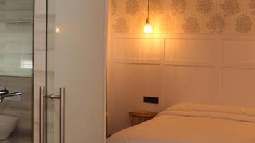 Habitación de hotel con cama, mesita de noche, espejo y zona de ducha.