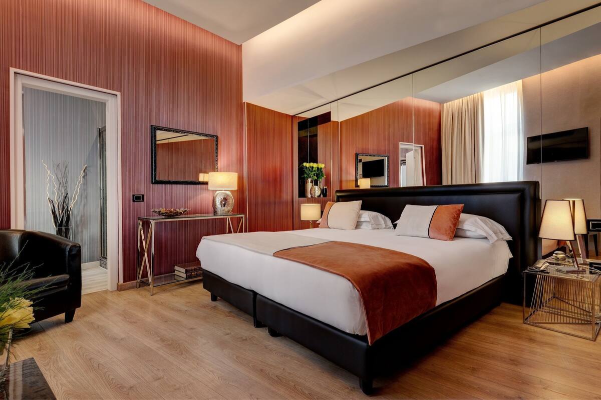 A modern hotel room with a large bed, a desk, a chair, and a TV.