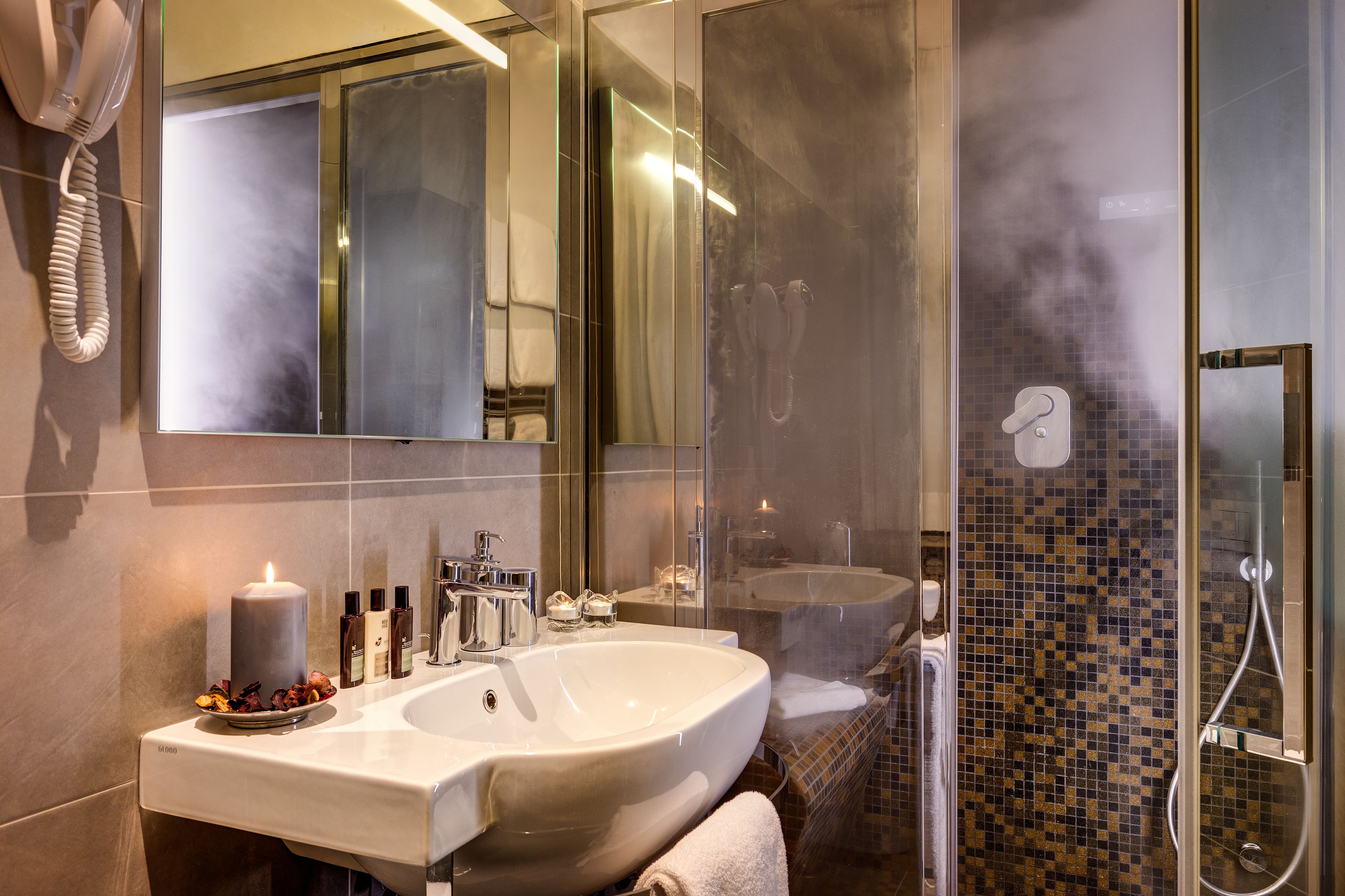 A modern bathroom with a large sink, a mirror, a glass shower enclosure, and a hairdryer on the wall.