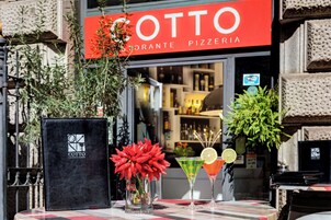 Un restaurante llamado Cotto con un letrero rojo, un atril para el menú y dos cócteles sobre una mesa.