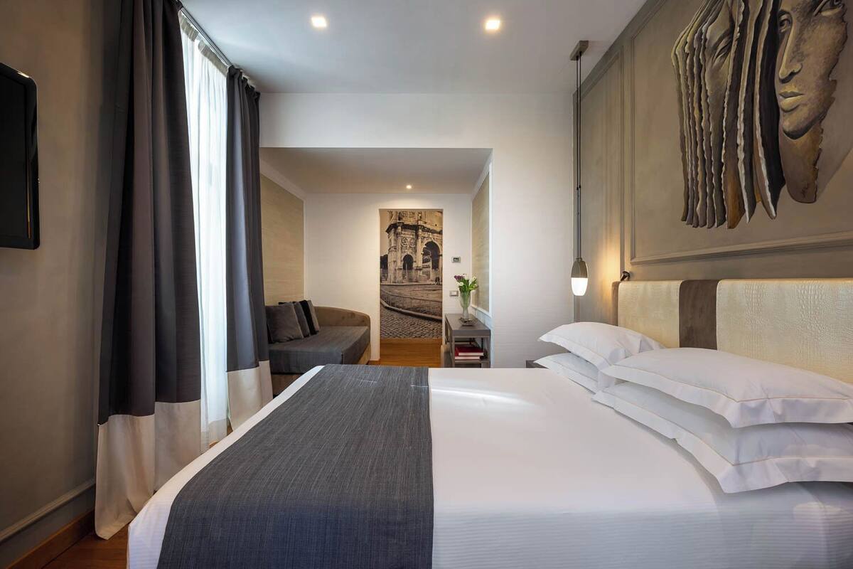 A hotel room with a large bed, a sofa, a nightstand, and a wall-mounted artwork.