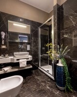 A modern bathroom with a large mirror, a glass-enclosed shower, a white sink, and a decorative vase with green foliage.