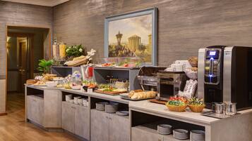 A buffet setup with various food items, a coffee machine, and a painting on the wall.