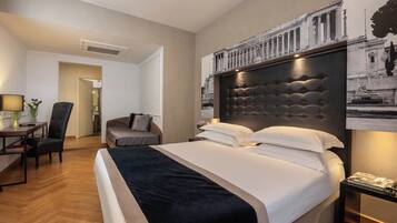 A hotel room with a large bed, a desk with a chair, and a nightstand with a lamp.