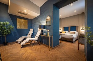 Una camera d'albergo moderna con un letto grande, un angolo salotto con due poltrone, un tavolino e una pianta in vaso.