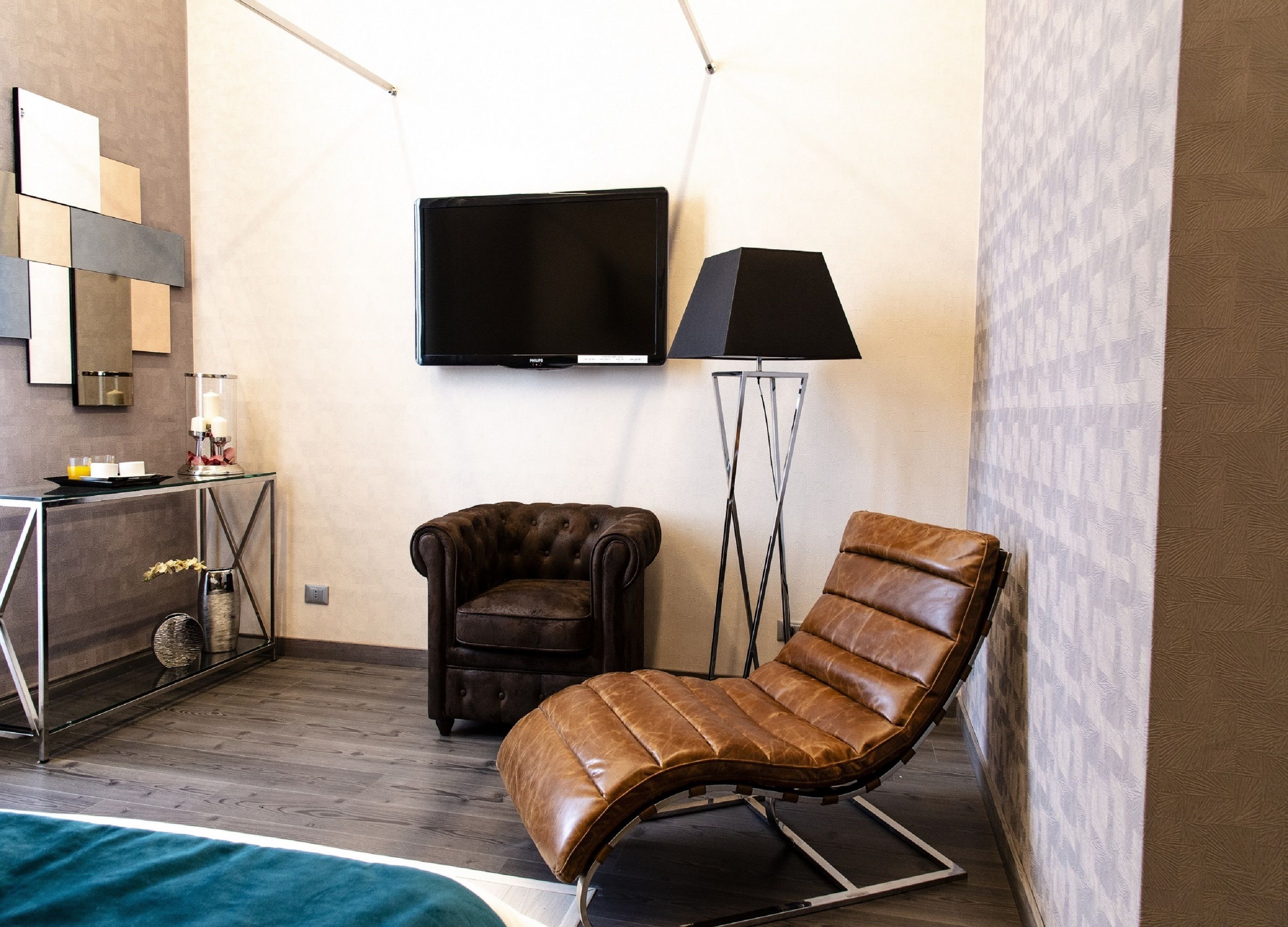 Une chambre d’hôtel moderne, dotée d’un fauteuil en cuir, d’un fauteuil capitonné, d’un téléviseur à écran plat et d’un lampadaire.