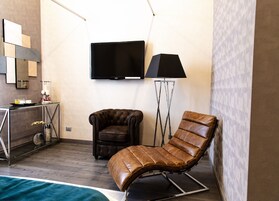 A modern hotel room with a leather armchair, a tufted armchair, a flat-screen TV, and a floor lamp.