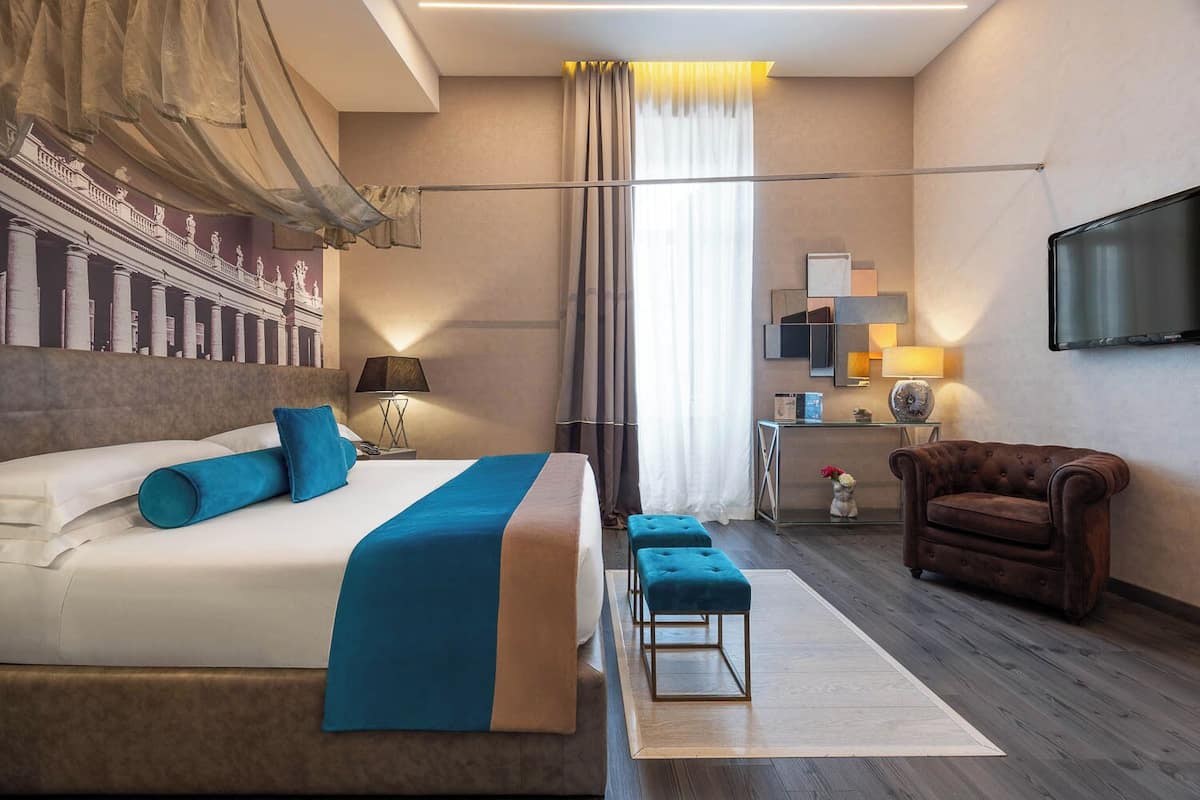 A modern hotel room with a large bed, a desk, a chair, and a TV.