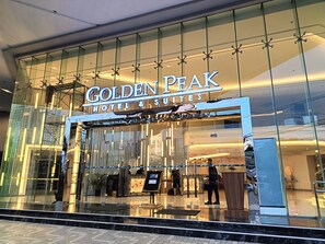 Fachada moderna de cristal del Golden Peak Hotel & Suites, con un letrero llamativo.