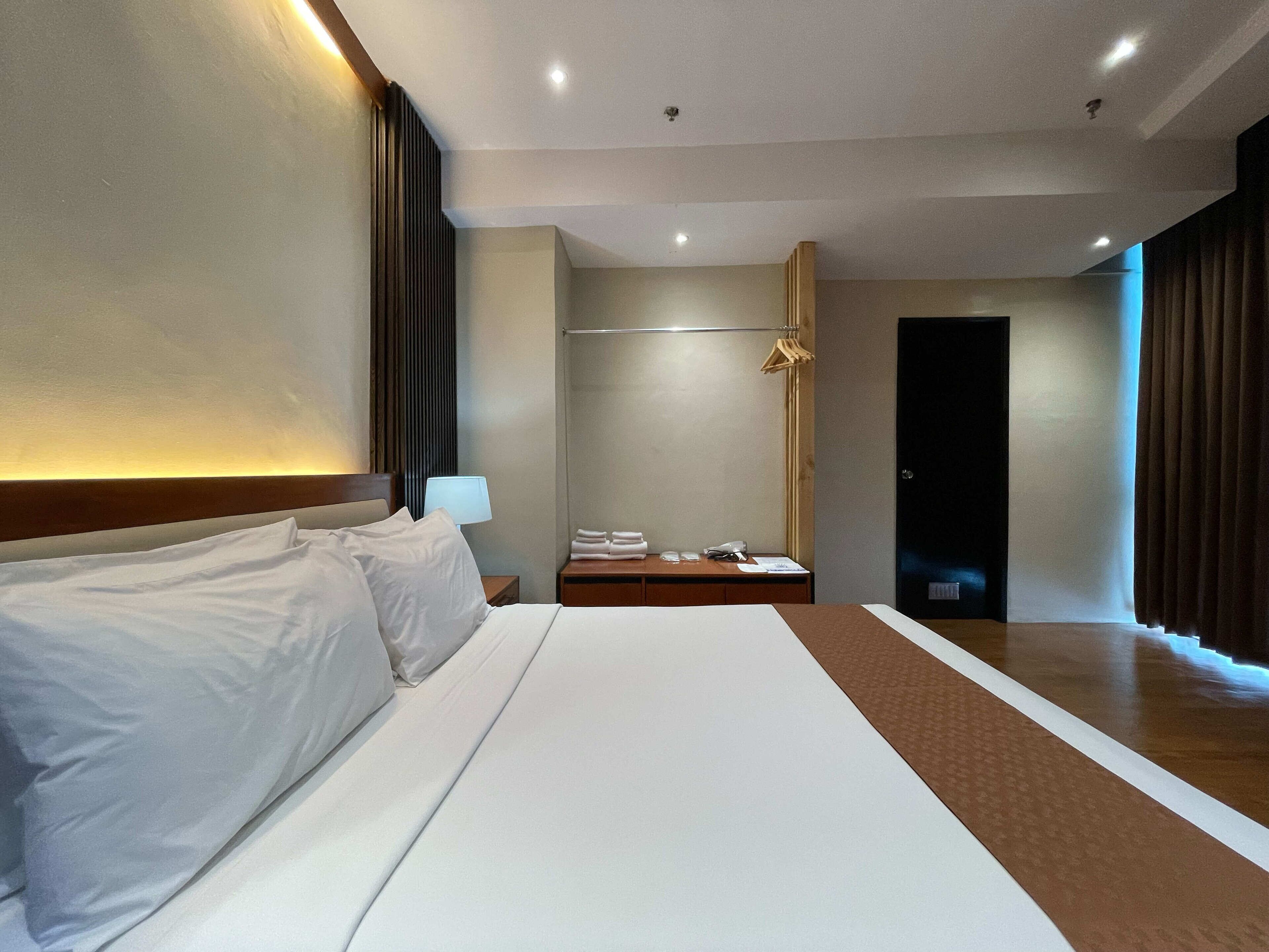 Una habitación de hotel con una cama grande, una mesita de noche con lámpara, un armario y una puerta.