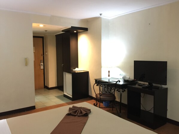 Habitación de hotel con cama, escritorio con computadora y televisión, una silla y una mesita con lámpara.