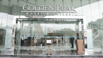 The exterior of the Golden Peak Hotel & Suites with a glass facade, a reception desk, and a signboard.