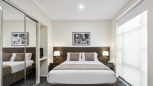 A hotel room with a large bed, bedside tables with lamps, a mirror, and framed pictures on the wall. - Quest Narre Warren (Narre Warren)