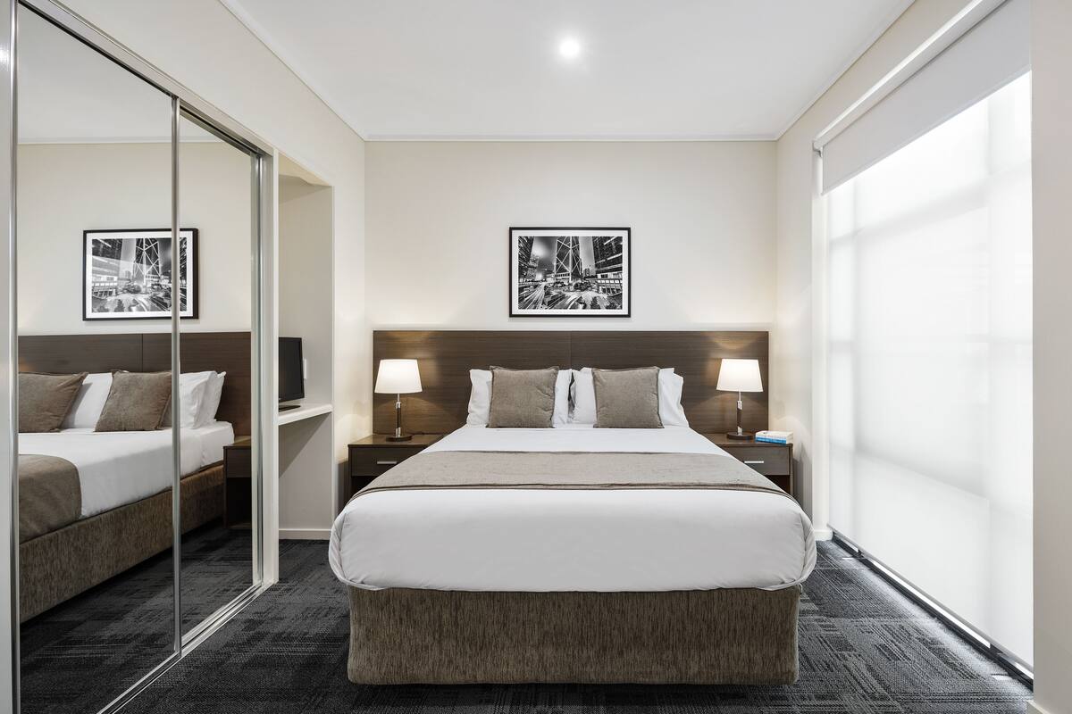 A hotel room with a large bed, bedside tables with lamps, a mirror, and framed pictures on the wall.