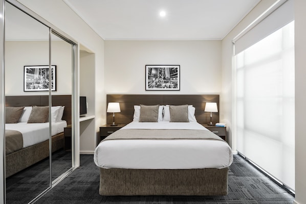 Habitación de hotel con una cama grande, mesitas de noche con lámparas, un espejo y cuadros en la pared.