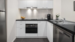 A modern kitchen with white cabinets, a black countertop, stainless steel appliances, and a vase with flowers. - Quest Narre Warren (Narre Warren)